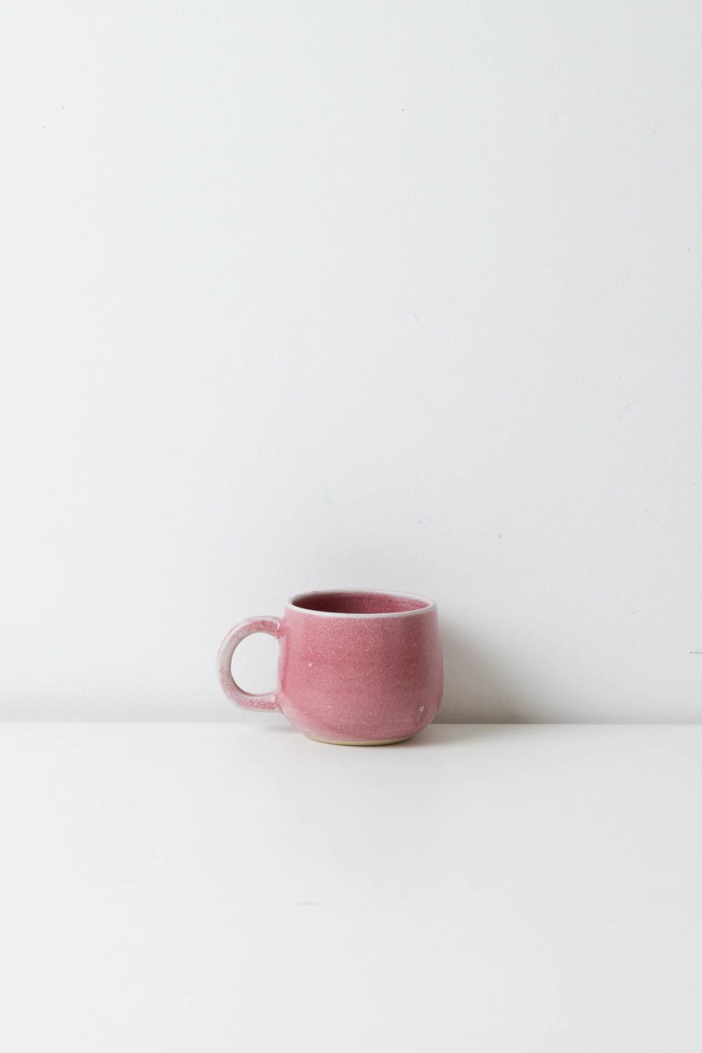 Caneca de cerâmica rosa fosco com alça larga, sobre bancada branca